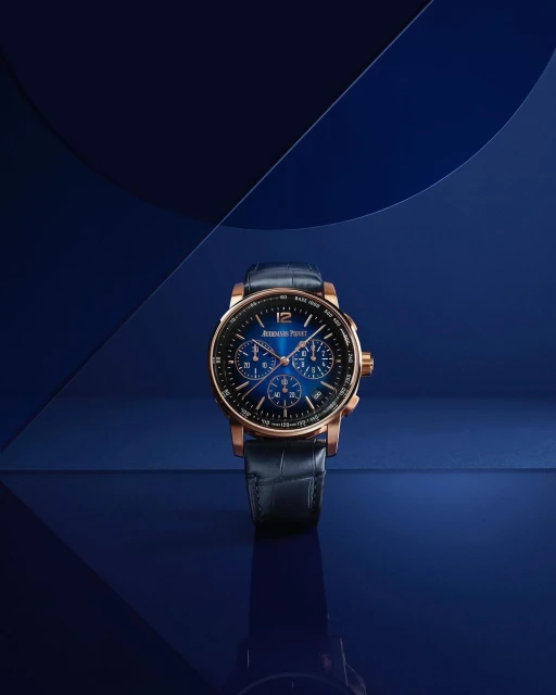 Elegant rose gold and blue Audemars Piguet wristwatch displayed on a reflective blue surface in a studio setting, product photography.