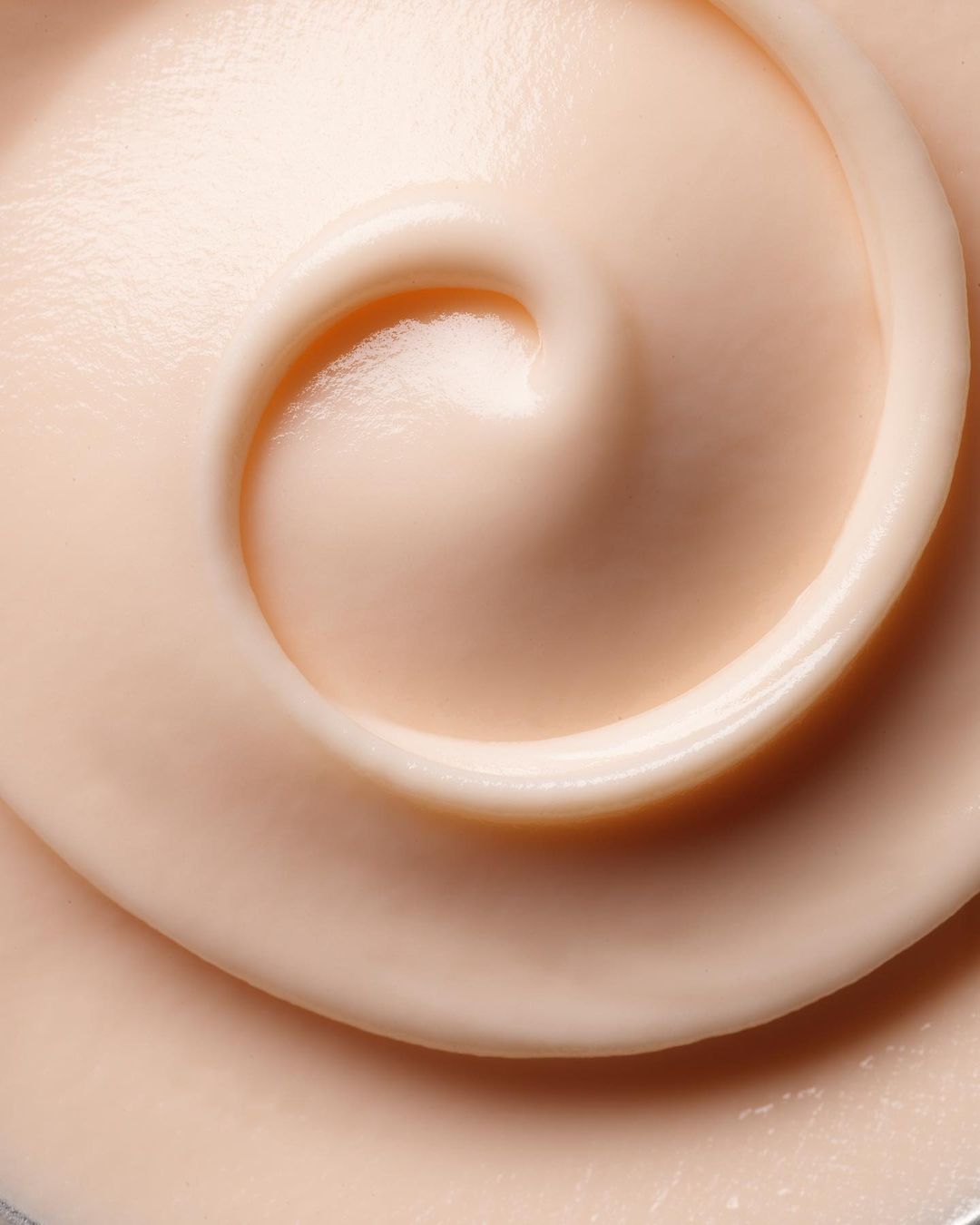 Close-up of a swirling pattern in a light peach-colored creamy substance, likely a facial cream or cosmetic product, smooth texture.