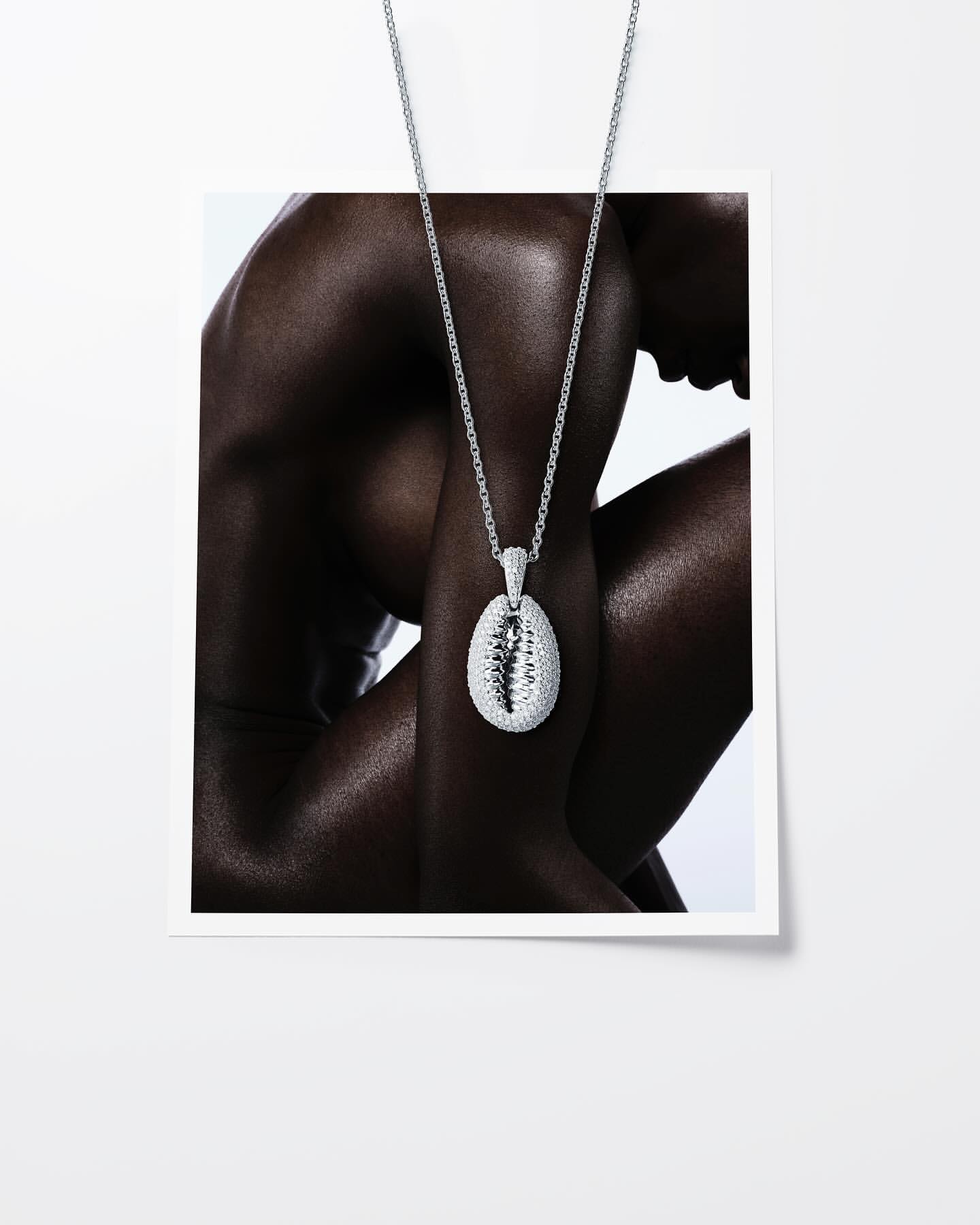 Glamorous fashion shot: A dark-skinned person wears a silver pendant necklace in a studio, accessorizing against a white background.