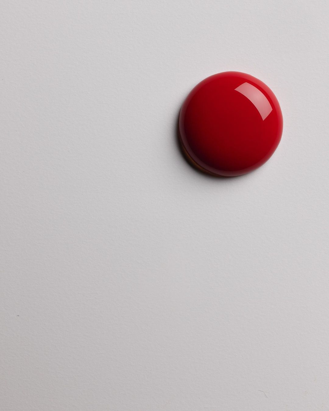 Close-up studio shot of a glossy, dome-shaped red candy or dessert with a smooth, reflective surface, presented on a white surface.
