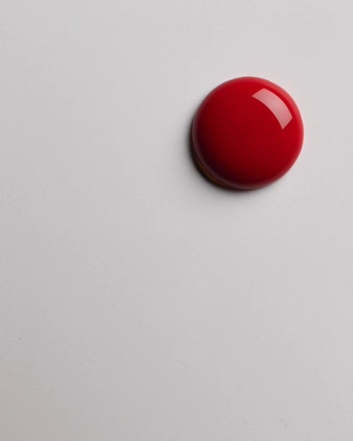 Close-up studio shot of a glossy, dome-shaped red candy or dessert with a smooth, reflective surface, presented on a white surface.