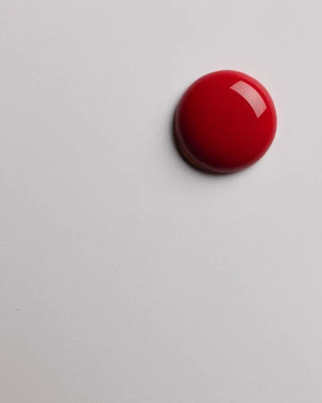 Close-up studio shot of a glossy, dome-shaped red candy or dessert with a smooth, reflective surface, presented on a white surface.