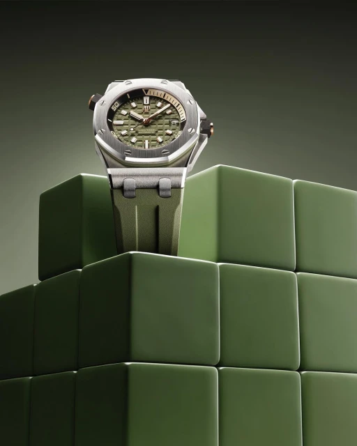 Silver wristwatch with an olive green face and band sits atop a geometric cube display against a graduated olive green background.