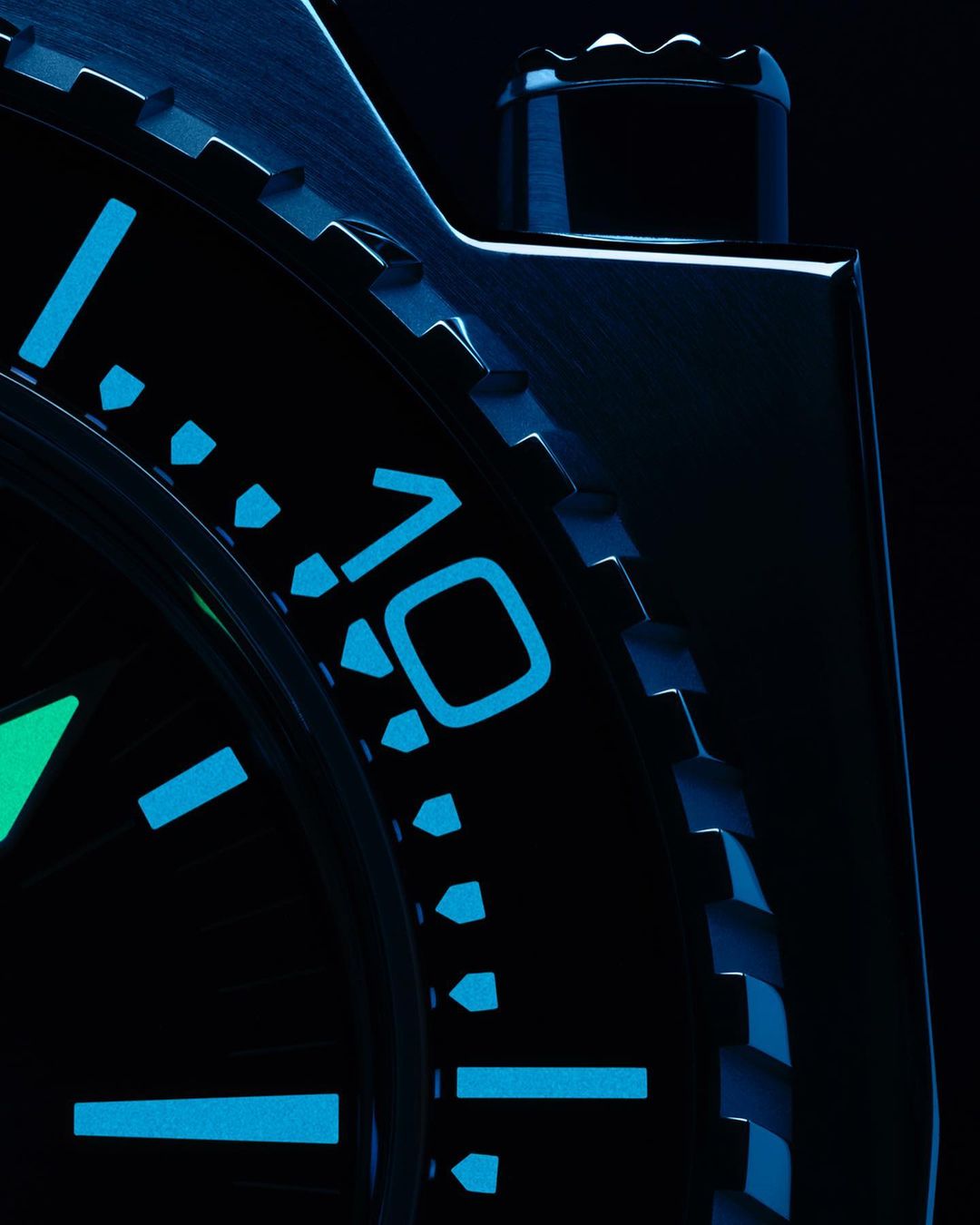 Close-up product shot of a black wristwatch featuring blue-glowing indices and numbers. Shot focuses on the watch's dial and bezel.