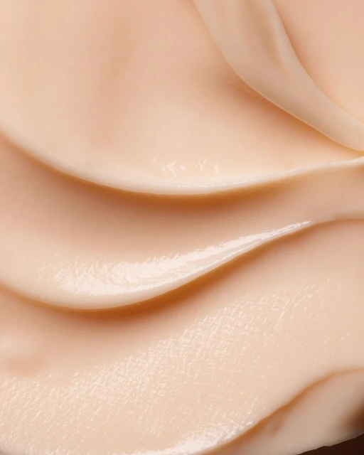 Close-up of a smooth, light-beige cream texture with wavy patterns. Abstract beauty and skincare product shot. Neutral, monochromatic color scheme.