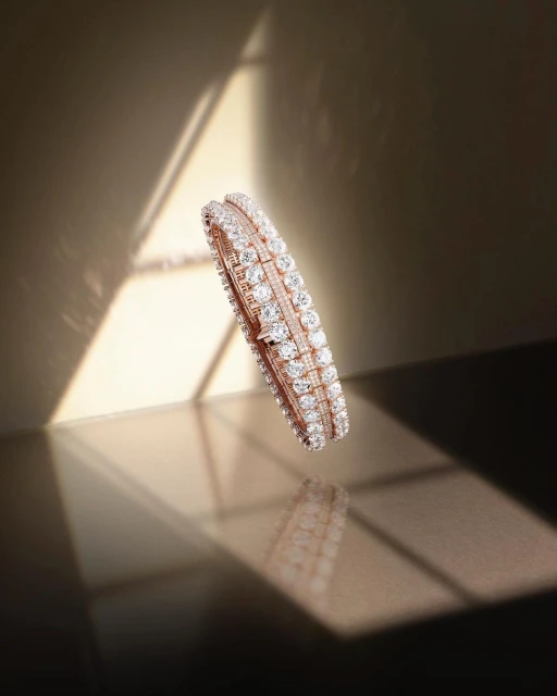 Elegant bangle bracelet with white gems and gold, reflecting light and shadow, is displayed against a neutral-tone backdrop indoors.