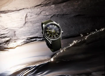 Green dial wristwatch with a textured green rubber strap positioned over a dark slate rock and water surface with splashing droplets.