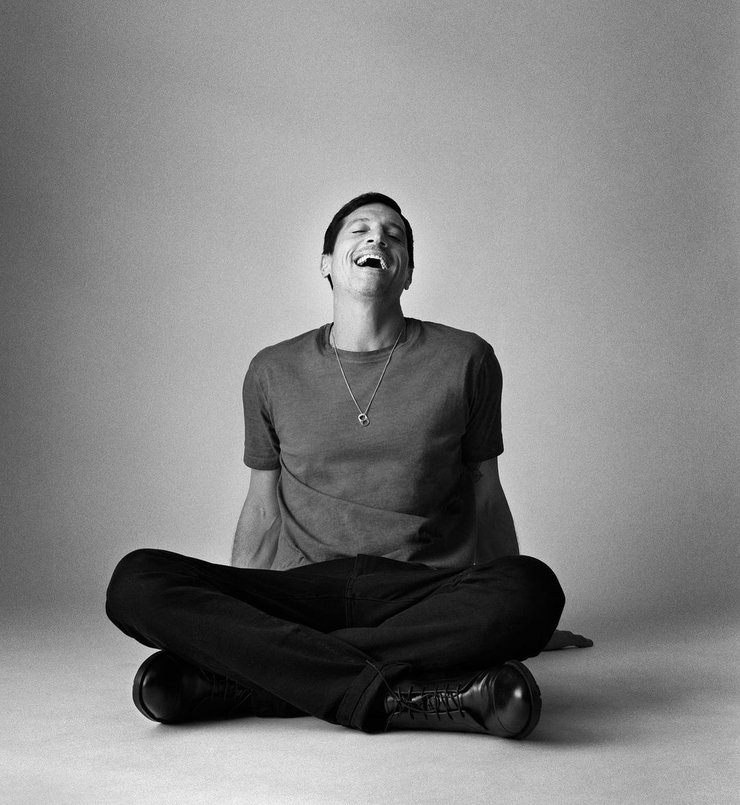 Man sitting cross-legged laughing in a monochrome studio portrait