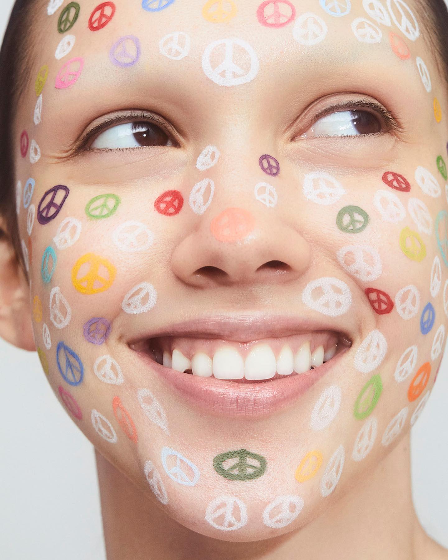 Close-up of a woman's face with colorful peace sign face paint. Beauty shot with vibrant symbols, fair skin, and a bright smile.