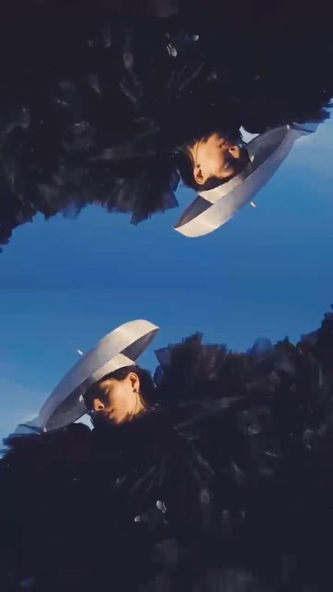 Two women face each other with large white hats on in front of a blurred blue sky background, an artistic style image.