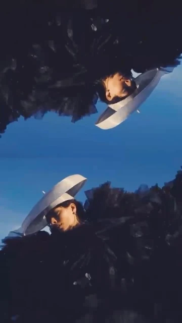 Two women face each other with large white hats on in front of a blurred blue sky background, an artistic style image.
