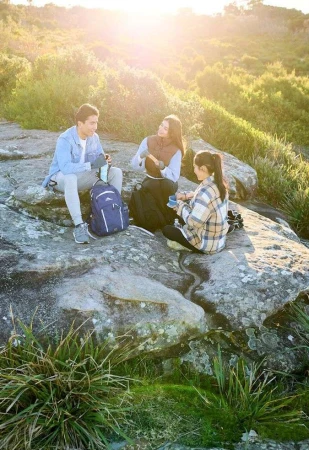 Three young friends resting on large grey rocks in a grassy natural landscape during bright sunny daylight