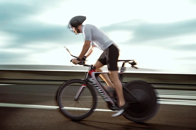 A cyclist races on a Specialized road bike along a highway, showcasing speed with motion blur against a cloudy sky and concrete barriers.