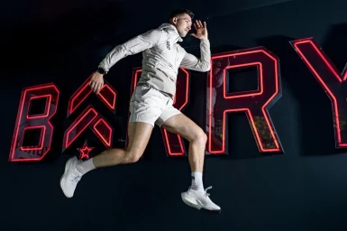 Man captured mid-air running past large illuminated red neon letters against a dark wall background