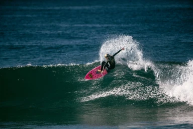 Surfer on a pink surfboard carving through an ocean wave with white water spray by Eric Yip