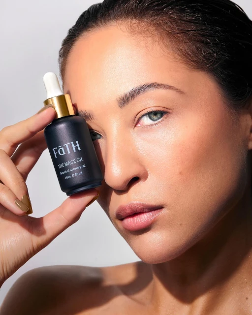 Close-up of a woman holding a black bottle of FATH The Mage Oil. Beauty shot with neutral background. Cosmetics advertisement.
