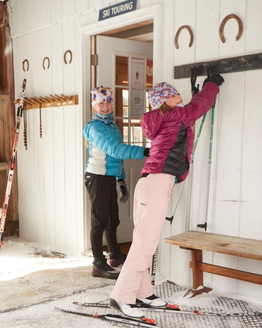Two young girls preparing for cross-country skiing in winter. One girl in a blue jacket helps the other, who wears a pink jacket, with her poles.