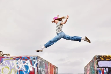 Young woman leaping mid-air between two graffiti-covered concrete blocks against an overcast sky
