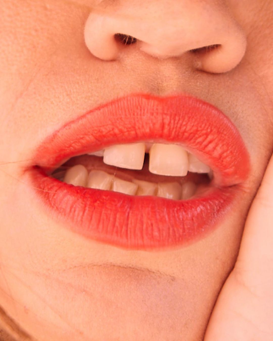 Close-up of a person's face featuring bright red lipstick, white teeth with a noticeable gap, and fair skin.