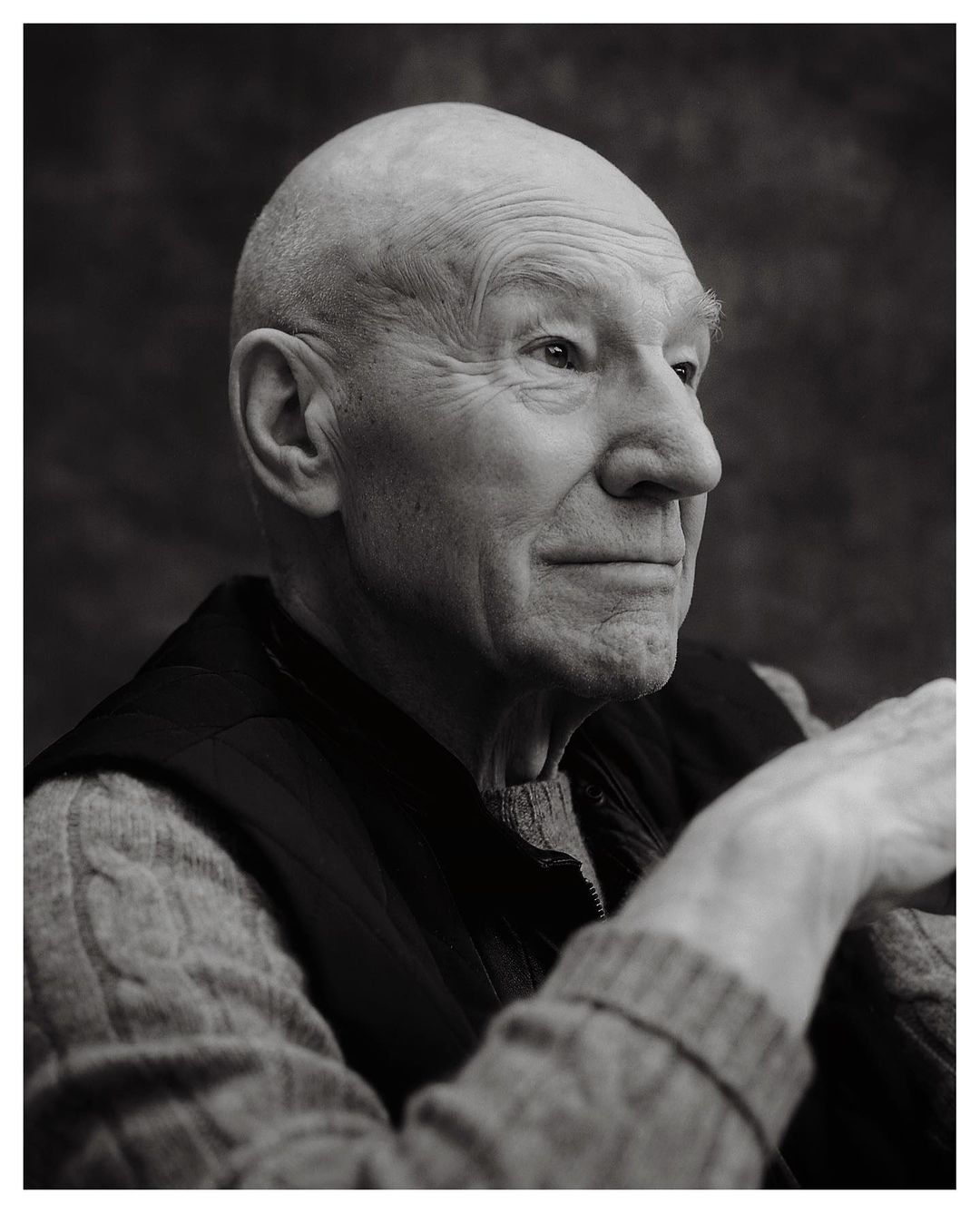 Portrait of a bald elderly man wearing a sweater and vest against a dark textured background photographed by Erik Carter