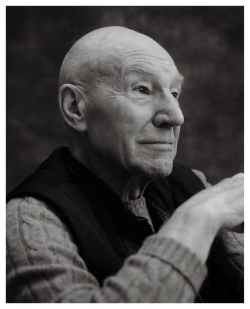 Portrait of a bald elderly man wearing a sweater and vest against a dark textured background photographed by Erik Carter