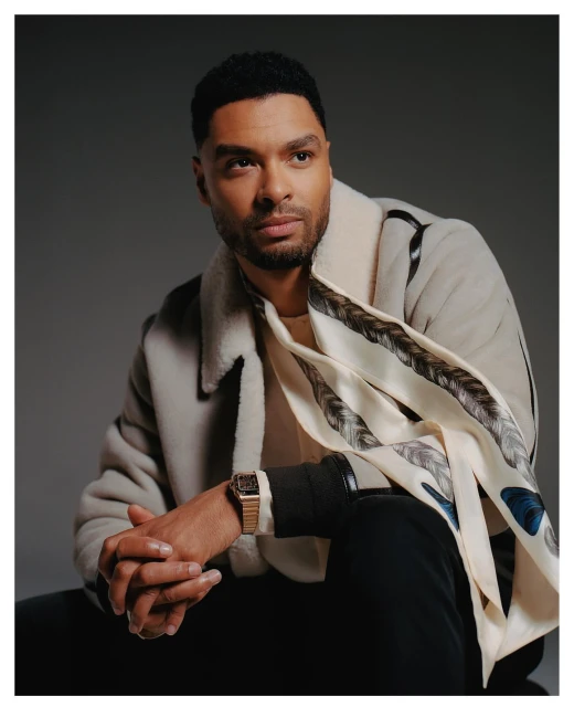 Portrait of a handsome adult male with dark hair, wearing a cream colored coat and scarf, looking off into the distance in a studio.
