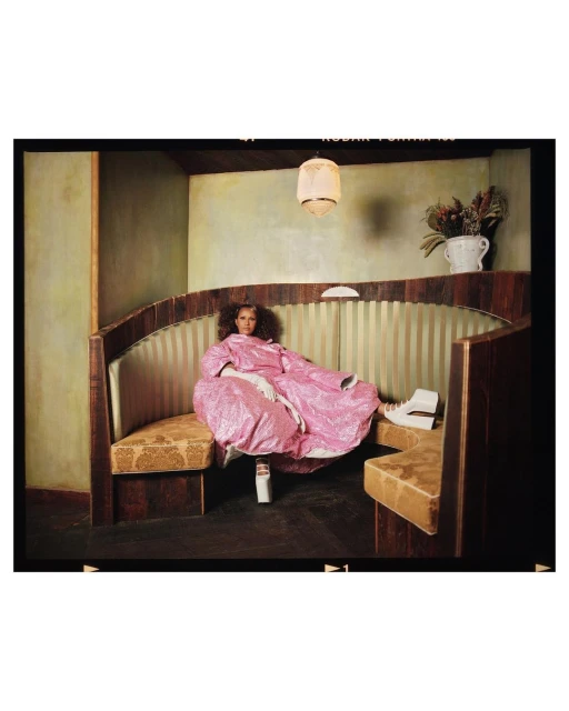 Woman in a pink robe poses in a vintage-style diner booth with white platform shoes, creating a unique fashion-forward image.