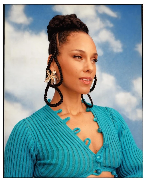 Close-up studio shot of a smiling adult female celebrity with braided hair wearing a turquoise, button-up top against a blue sky backdrop.