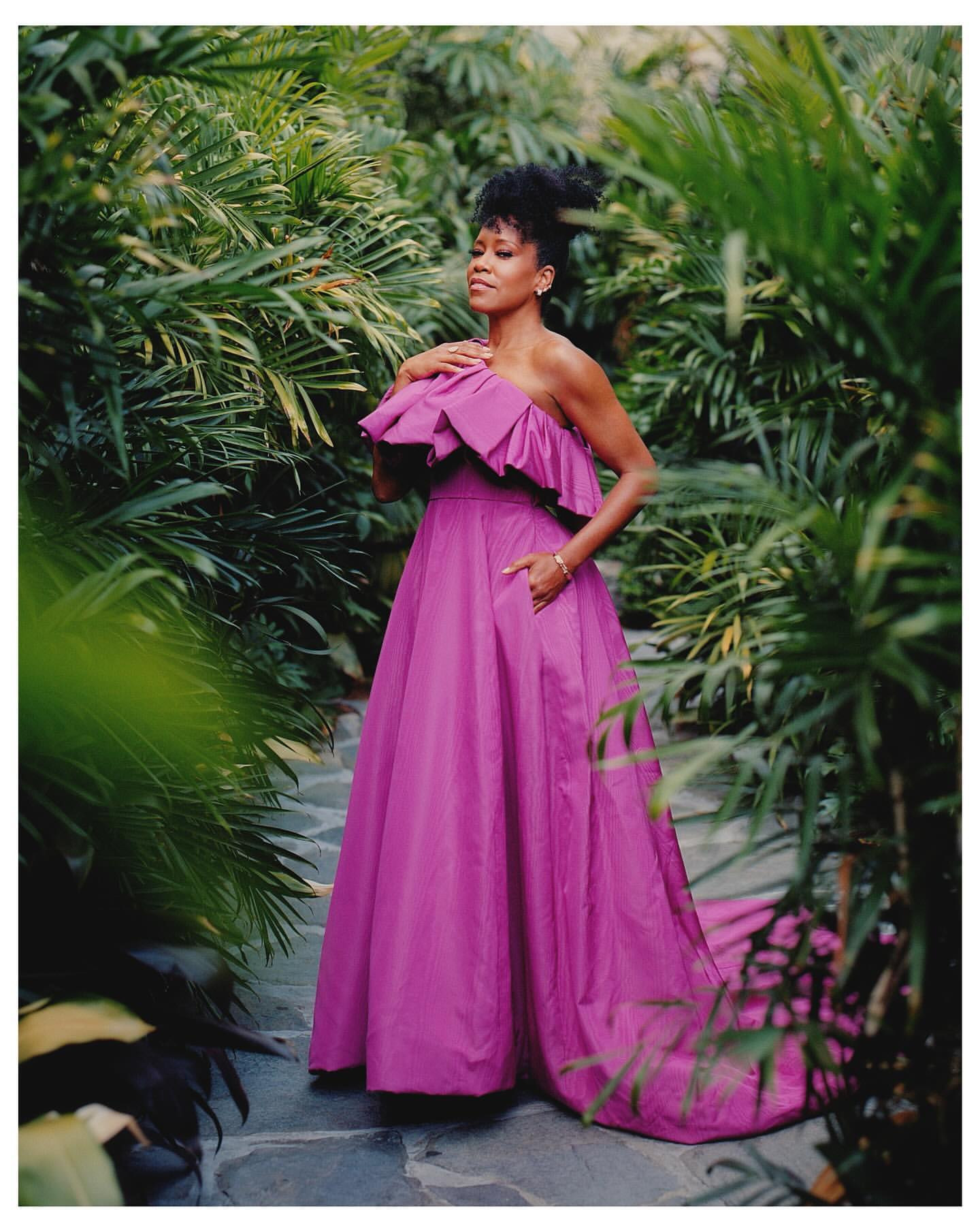 Elegant woman in a ruffled magenta gown poses in lush greenery. Fashion shoot with a botanical backdrop, garden setting.