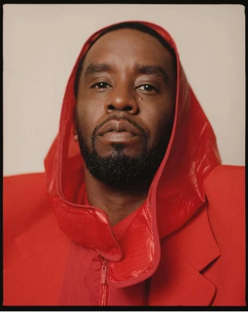 Close-up portrait of an African American male with a beard, wearing a red hooded jacket, against a neutral beige background.