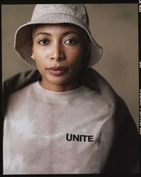 Portrait of a Black woman with short hair wearing a bucket hat and a sweatshirt with UNITE text by photographer Erik Carter