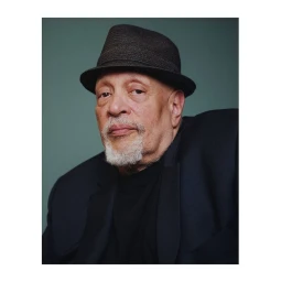 Portrait of a man wearing a dark fedora and jacket against a plain muted teal background