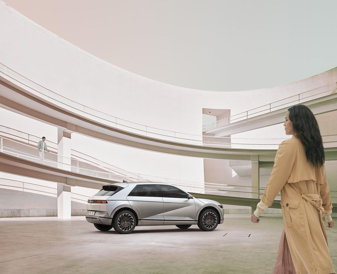 Silver Hyundai Ioniq 5 electric car showcased inside a modern architectural building with a woman walking by.