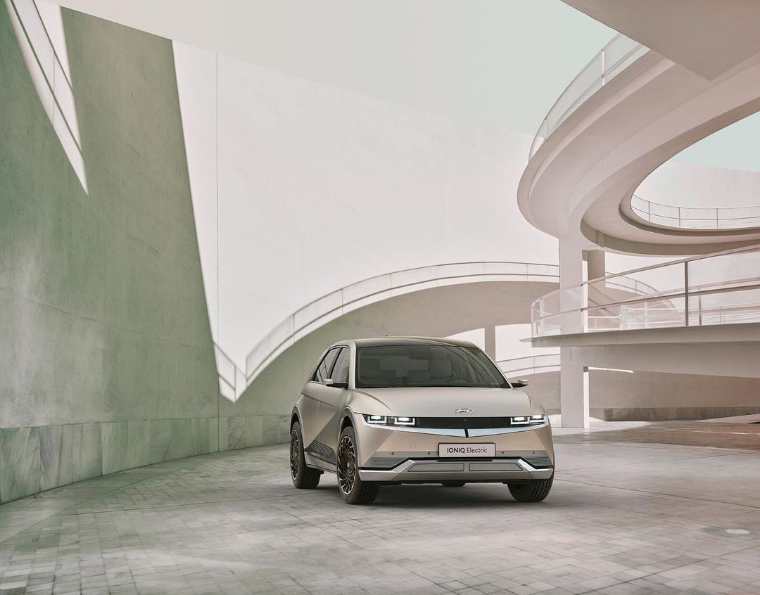 A modern silver Hyundai IONIQ 5 electric car is parked on a paved surface with a contemporary white architectural background.
