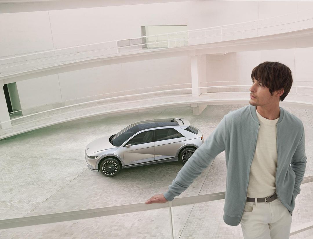 Silver Hyundai Ioniq 5 electric car parked inside a modern white building with a man standing nearby looking off into the distance.