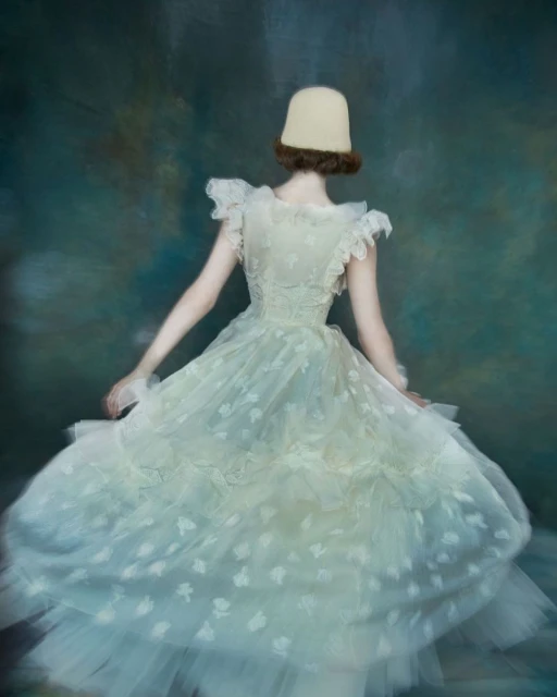 Back view of a person in a vintage white dress with a flower pattern, and a beige hat against a blurry teal textured backdrop.