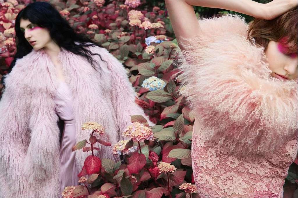 Two women in pink faux fur coats pose amidst hydrangeas. Soft, diffused lighting. Fashion editorial. Beauty shot. Dreamy and surreal aesthetic.