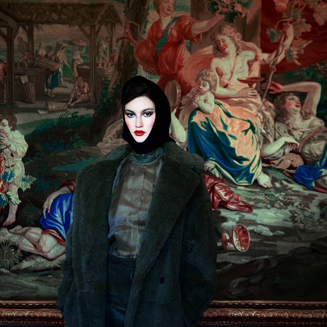 Woman in a black headscarf and green coat stands in front of a large tapestry with figures in a classical scene.