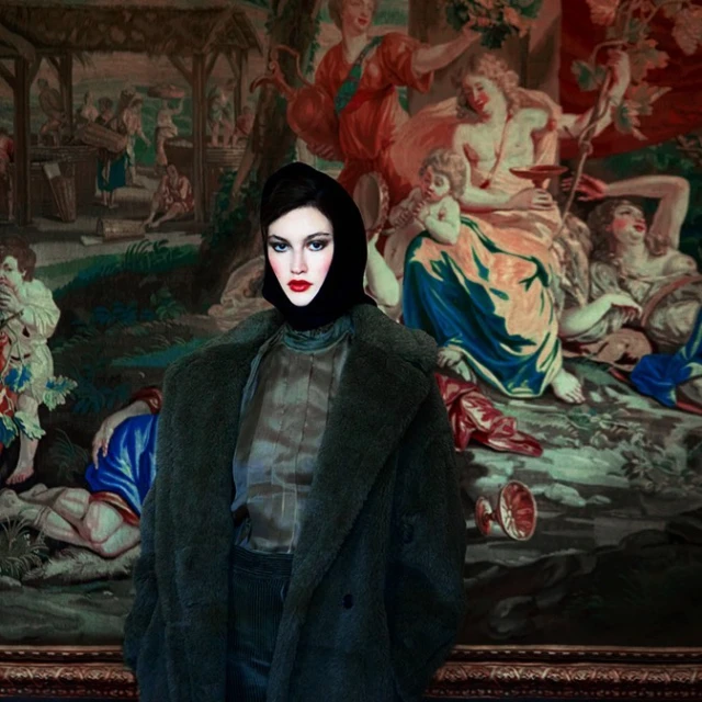 Woman in a black headscarf and green coat stands in front of a large tapestry with figures in a classical scene.