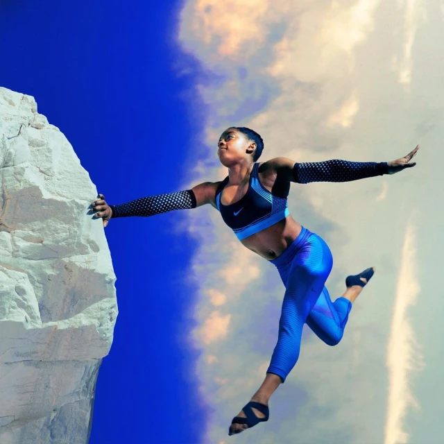 Athletic African-American woman leaps from rock cliff against a vibrant blue sky with wispy clouds wearing blue athletic wear, sleeves, and open toe sandals.