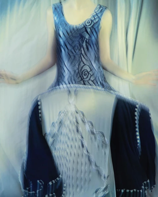 Abstract fashion shot featuring a blurred female model wearing a sleeveless blue dress with decorative swirls against a soft white background.