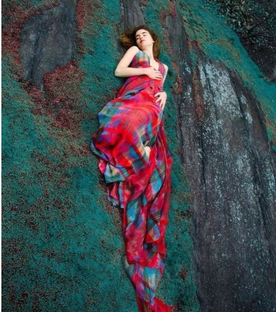 A woman lying on a moss-covered rock wearing a vibrant red plaid dress, photographed by Erik Madigan Heck.