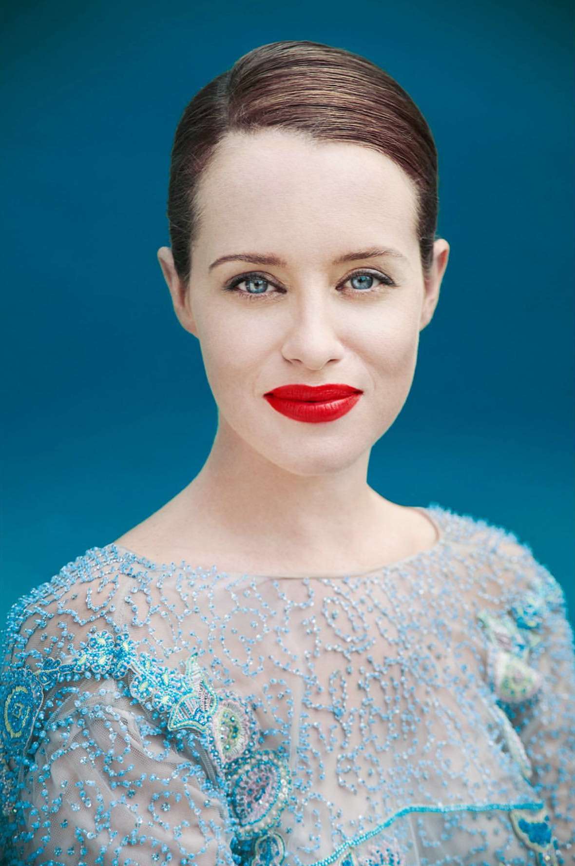 Close-up portrait of a woman with red lips and blue eyes wearing an embellished blue dress against a textured blue background.