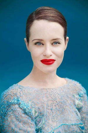 Close-up portrait of a woman with red lips and blue eyes wearing an embellished blue dress against a textured blue background.