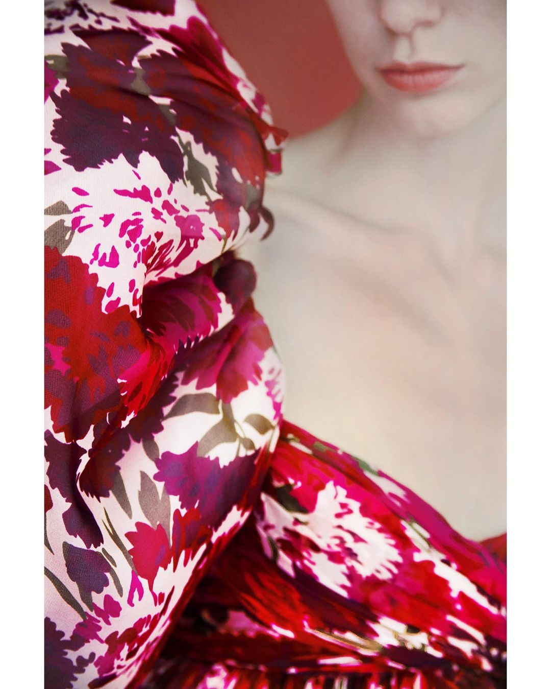 Close-up fashion shot of an adult female model with fair skin, wearing a red and pink floral-patterned dress. Studio shot with red background.