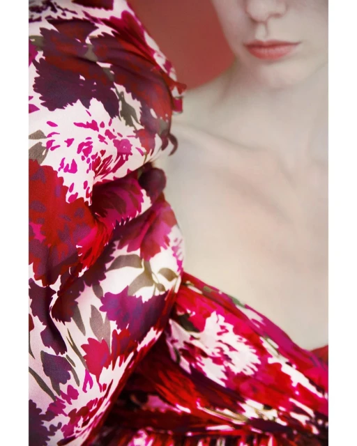 Close-up fashion shot of an adult female model with fair skin, wearing a red and pink floral-patterned dress. Studio shot with red background.