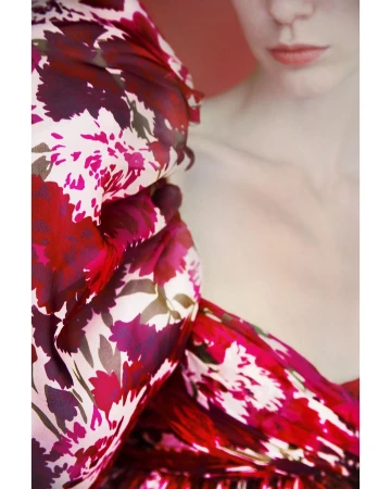 Close-up fashion shot of an adult female model with fair skin, wearing a red and pink floral-patterned dress. Studio shot with red background.