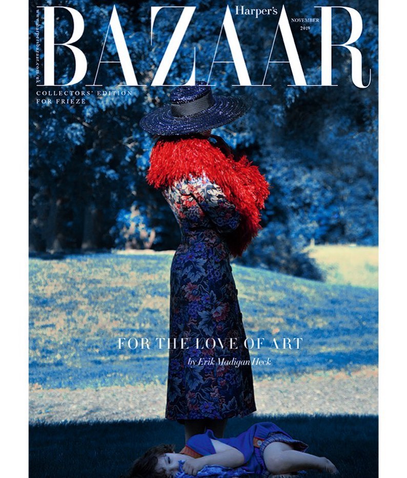 Fashion magazine cover: A woman in a floral dress, red boa and matching hat stands on grass in front of a blue-toned forest scene.