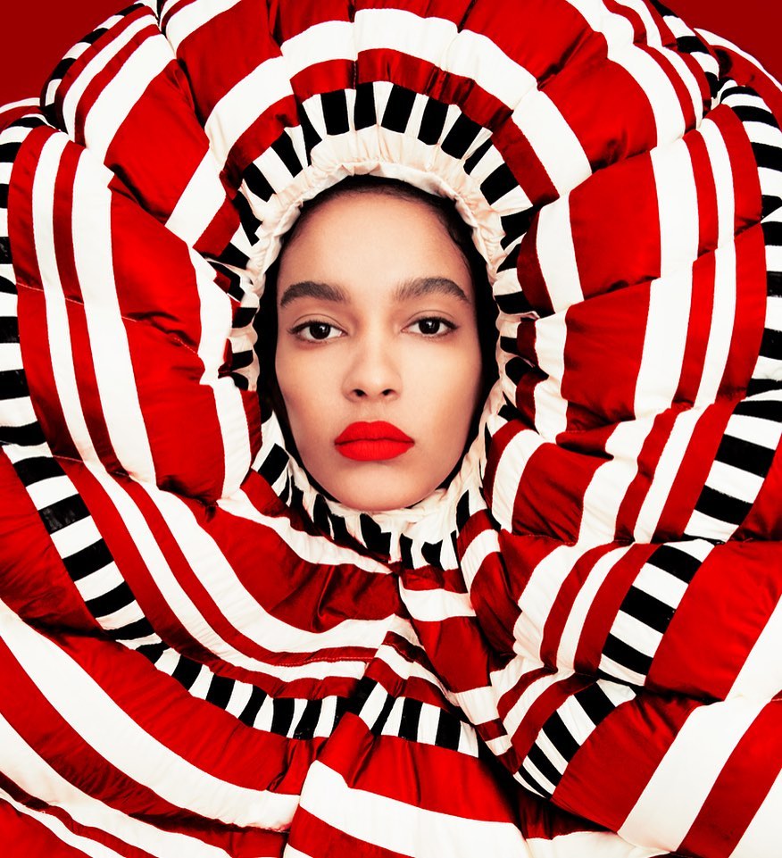 Portrait of a beautiful mixed race adult female wearing a puffy white and red striped coat with matching hood and bold red lipstick.