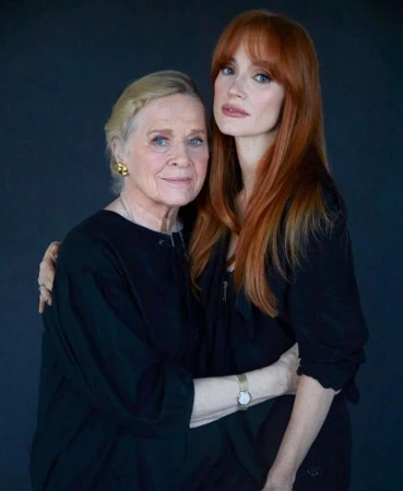 Two women with red and blonde hair wearing black clothing posing against a dark background in a portrait photograph by Erik Madigan Heck
